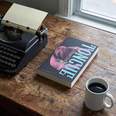 TONGUE: A Cognitive Hazard lying beside a vintage typewriter on a wooden desk